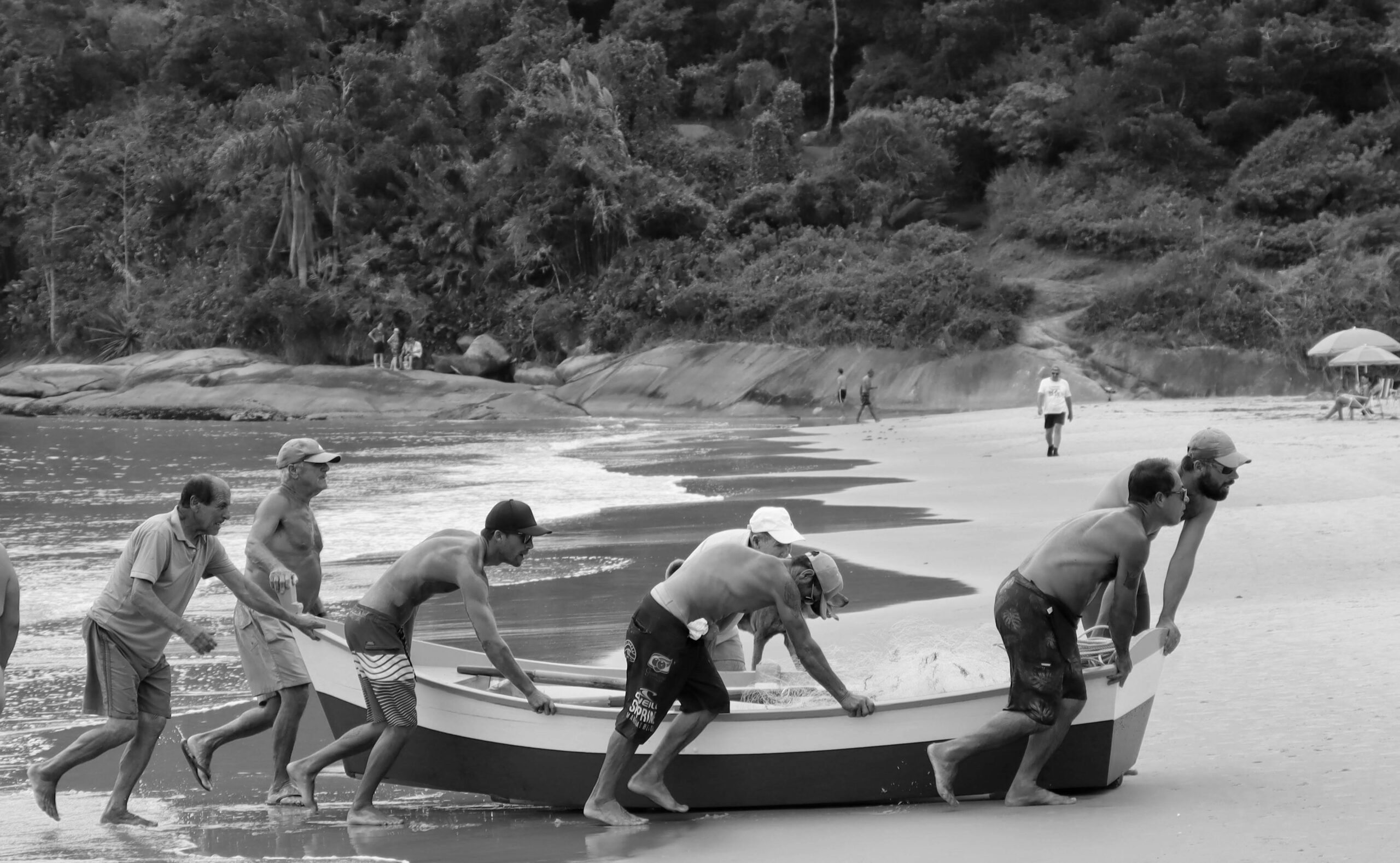 Black and white photo of men pushing a boat on a Brazilian beach. Teamwork and effort.